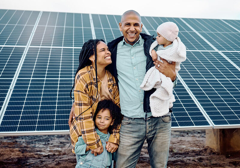 Black family with kids standing in front of solar panels and smiling